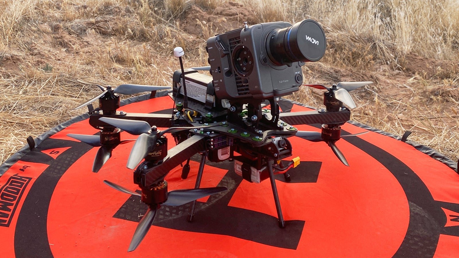 Heavy-lift FPV cinelifter drone carrying a full-frame cinema camera on an orange landing pad