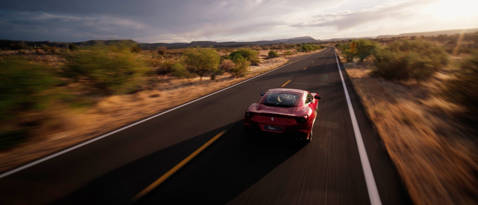 FPV drone tracking shot of a red Ferrari Portofino driving at speed through a desert landscape, captured with a Sony FX6